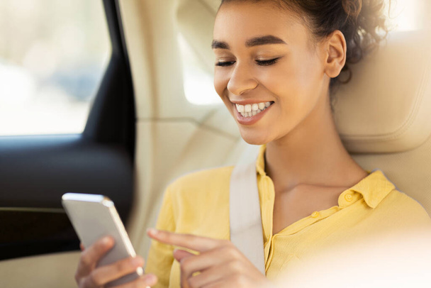 African American Girl Using Smartphone Sitting In Car During Ride - 写真・画像
