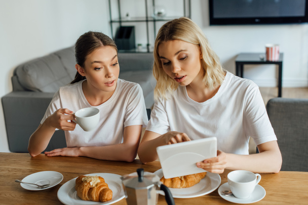 Focus selettivo delle sorelle che utilizzano tablet digitale durante la colazione in cucina
  - Foto, immagini