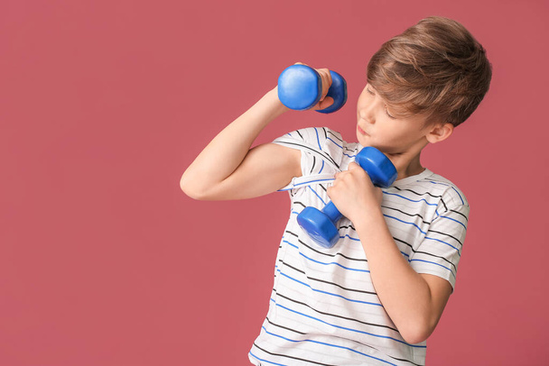Sportlicher kleiner Junge mit Hanteln auf farbigem Hintergrund - Foto, Bild