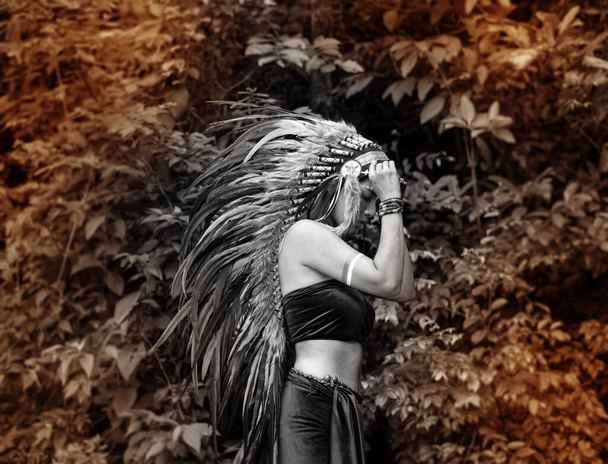 Красивая женщина, поднимающая головной убор, сделанный из перьев птиц. раскрашенный синий цвет на щеке, портрет позирующей модели, джунгли в лесу, черно-белый тон, размытый свет вокруг
 - Фото, изображение