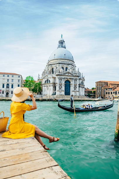 женщина в желтом сарафане, сидящая на пирсе с видом на Гранд-канал Венеция Летние каникулы в Италии. копировальное пространство - Фото, изображение