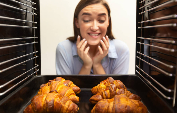 Frohes Mädchen schaut sich leckere frische Croissants im Ofen an - Foto, Bild