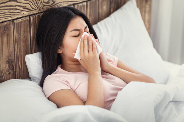 ベッドに横たわっ組織で鼻を吹いて病気の中国人女性 - 写真・画像