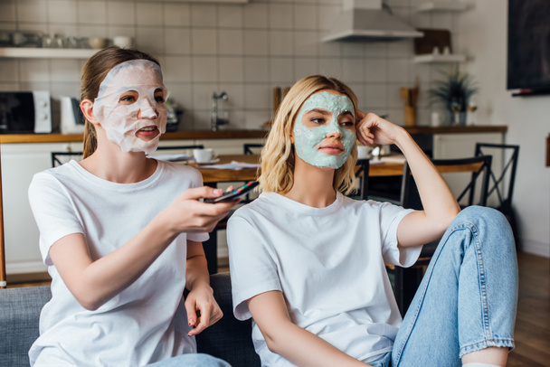Sisters in face masks watching tv on couch at home  - Фото, зображення