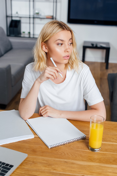 Beautiful freelancer holding pen near notebook, laptop and glass of orange juice on table  - Photo, Image