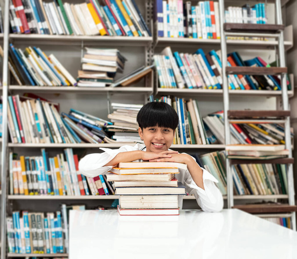 Young teenager put her chin on book stacked,prepare for searching data,with happy feeling,at library - Photo, Image