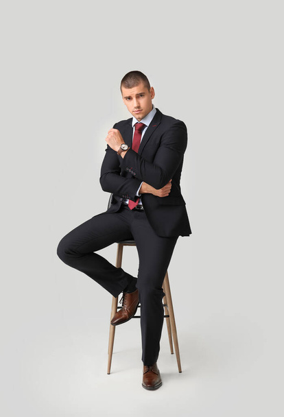 Przystojny młody człowiek w eleganckim garniturze siedzi na krześle na jasnym tle - Zdjęcie, obraz