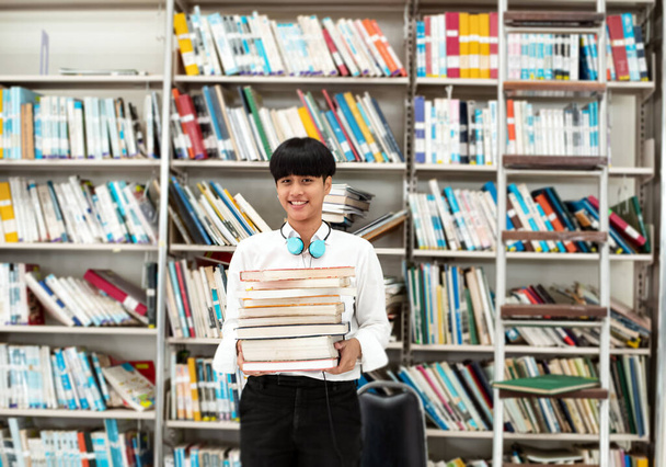 Young teenager holding books in hand,prepare for searching data,with happy feeling,at library,blurry light around - Photo, Image