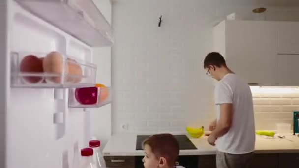 Camera inside the kitchen refrigerator: a boy opens the refrigerator door, looks inside. Man cooks in the kitchen - Filmati, video