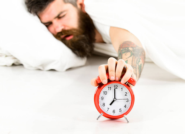 Guy with sleepy face holds alarm clock. - 写真・画像