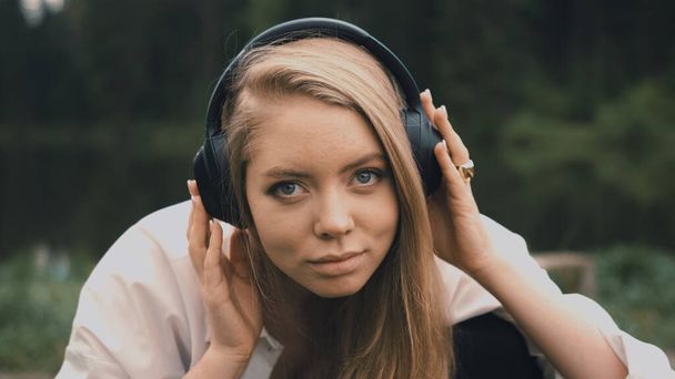 Beautiful young blonde woman with natural appearance listening to music on black headphones - Фото, зображення
