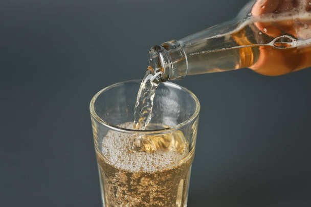Pouring of apple cider into glass on grey background - Photo, Image