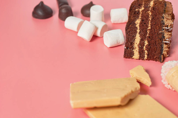 Pieces of chocolate cake near different sweets lies on pink table. Copy space - Photo, Image