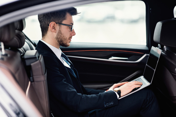Fiatal üzletember használja laptop luxus autó - Fotó, kép