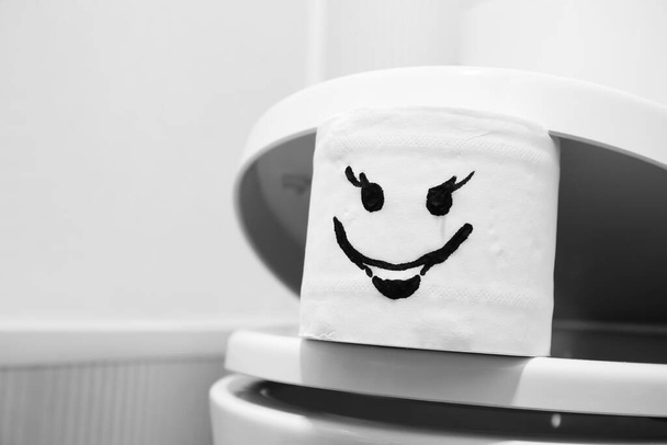 Rolo de papel higiênico com rosto desenhado no banheiro
 - Foto, Imagem