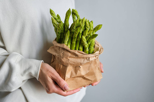 Green asparagus in the hands of a girl. Bunch of ripe fresh asparagus. Healthy organic food. Cooking in home. Natural vitamins, raw ingredient for eating. Handpicked bio asparagus - Foto, Imagem