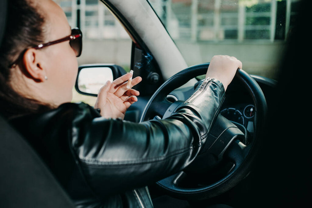 Νεαρή γυναίκα καπνίζει ένα τσιγάρο ενώ οδηγεί ένα αυτοκίνητο, έννοια μεταφοράς - Φωτογραφία, εικόνα
