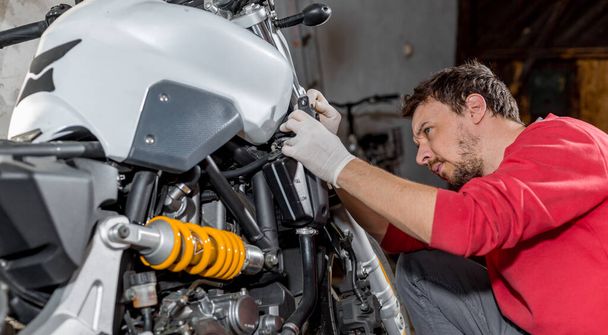 Opravář mechanik provádějící údržbu nebo opravy, upevnění na motocykl, motocykl, servisní středisko - Fotografie, Obrázek