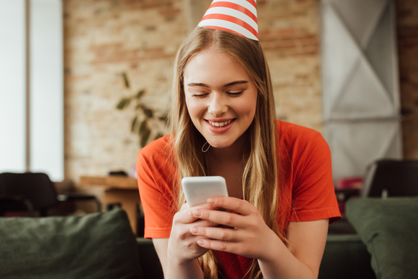 cheerful young woman in party cap using smartphone - Foto, afbeelding
