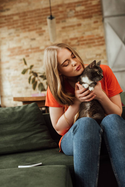 attractive young woman holding in arms cute cat near smartphone on sofa - Foto, Imagem