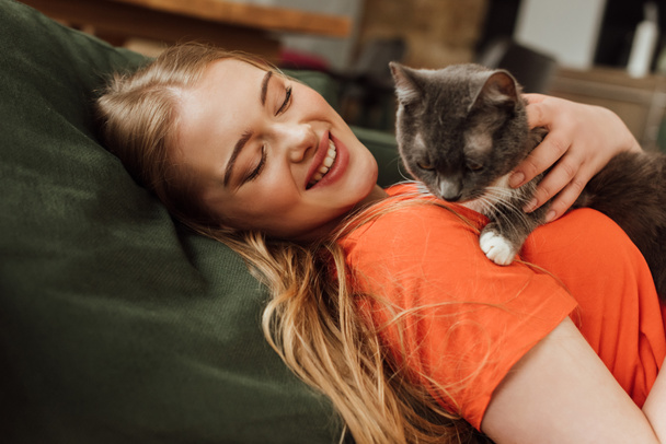 cheerful young woman looking at cute cat in living room  - Foto, Imagem