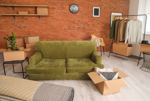 Cardboard boxes with belongings and sofa in new flat on moving day - Photo, Image