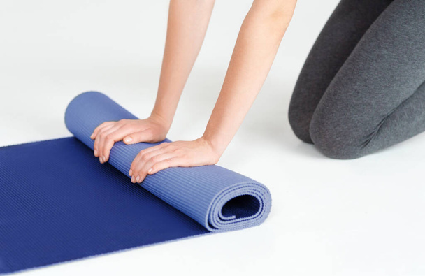 Closeup of young woman rolling her yoga mat on white background - Foto, Bild