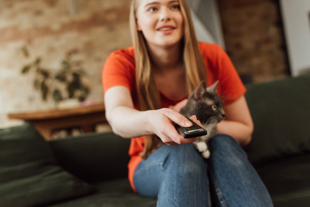 selective focus of happy girl holding remote controller near cute cat  - Foto, imagen