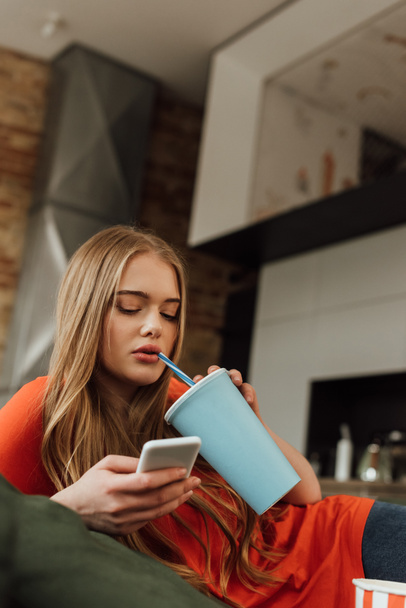 young woman holding paper cup with soda and using smartphone at home - Fotoğraf, Görsel