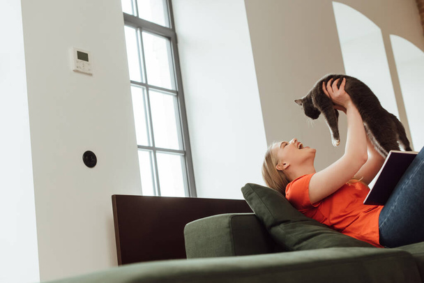 selective focus of excited young woman holding in arms cute cat in living room  - Foto, Imagem