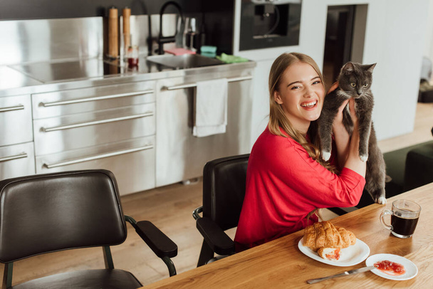 Genç ve mutlu bir kadın lezzetli bir kahvaltıda sevimli bir kedi tutuyor.  - Fotoğraf, Görsel