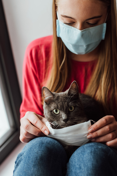 joven mujer en médico máscara sentado con lindo gato
 - Foto, imagen