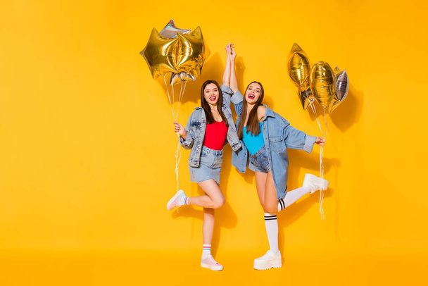 Full length body size view of nice attractive lovely pretty fashionable cheerful cheery girls holding in hands helium balls dancing isolated on bright vivid shine vibrant yellow color background - Фото, изображение