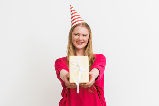 selective focus of cheerful girl in party cap holding gift isolated on white  - Fotoğraf, Görsel