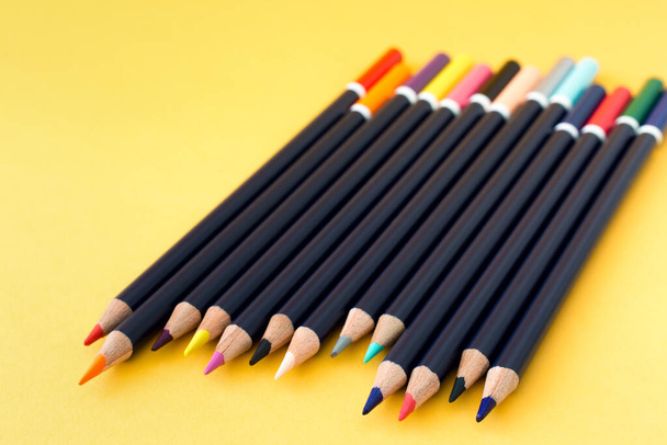 Renkli kalemler sarı arka planda kaotik bir şekilde yatar. Çizim, sanat, öğrenim, okul, iş konsepti. - Fotoğraf, Görsel