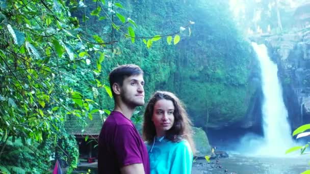 Preciosa joven con su novio de pie cerca de la cascada, concepto de viaje  - Metraje, vídeo