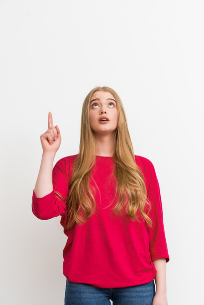 mujer sorprendida señalando con el dedo mientras mira hacia arriba aislado en blanco
 - Foto, imagen