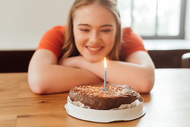 selective focus of cheerful girl looking at burning candle on delicious birthday cake  - Fotoğraf, Görsel