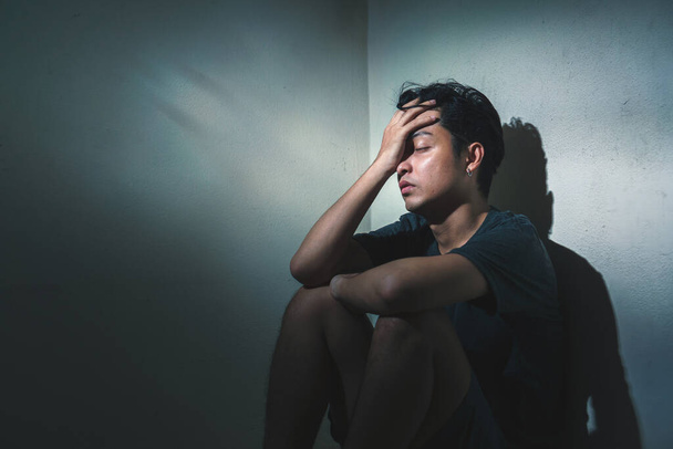 PTSD Conceito de saúde mental, Jovem deprimido asiático homem sentado sozinho no quarto escuro com ambiente de baixa luz, foco seletivo
. - Foto, Imagem