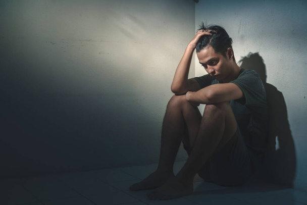 Junger depressiver asiatischer Mann, der allein in einem dunklen Raum mit wenig Licht sitzt, selektiver Fokus, PTBS-Konzept für psychische Gesundheit. - Foto, Bild