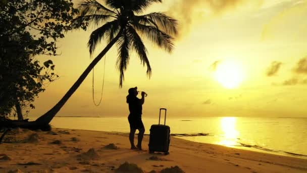 Kadın gün batımında elinde bavulla tropikal sahilde duruyor. - Video, Çekim