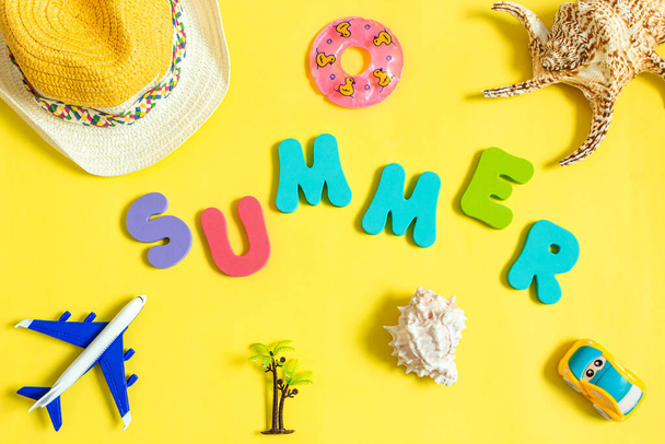 Airplane model, seashell, toy car, straw hat and word SUMMER made of color letters on yellow background. Concept of travel and vacation. Top view, flat lay. - Foto, immagini
