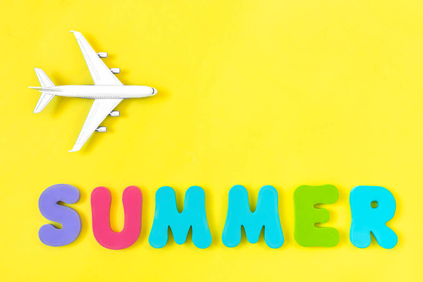 Modello aereo e parola ESTATE fatta di lettere colorate su sfondo giallo. Concetto di viaggio e vacanza. Vista dall'alto, disposizione piatta, spazio di copia
. - Foto, immagini