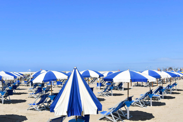 Offene Sonnenschirme und gut gefüllte blau-weiße Sonnenliegen am Sandstrand ohne Menschen - Foto, Bild