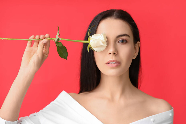 Όμορφη νεαρή γυναίκα με τριαντάφυλλο στο φόντο χρώμα - Φωτογραφία, εικόνα