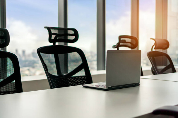 laptop na mesa na sala de reuniões com grandes janelas e vista da torre da cidade com céu desfocado, foco seletivo
. - Foto, Imagem