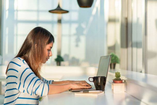 Jovem mulher asiática trabalhando em um laptop com beber café e sentar em casa escritório
. - Foto, Imagem