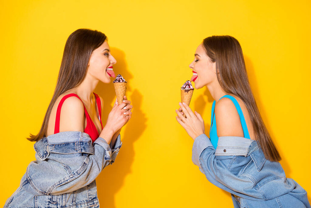 Profile side view portrait of her she nice attractive lovely pretty cheerful cheery haired girls licking icecream having fun isolated on bright vivid shine vibrant yellow color background - Valokuva, kuva