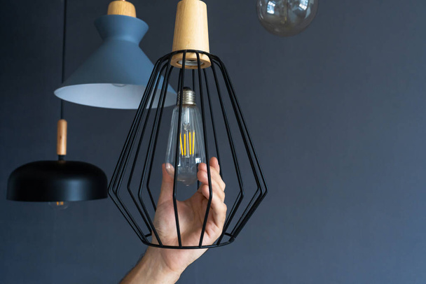 Close-up. A hand changes a light bulb in a stylish loft lamp. Spiral filament lamp. Modern interior decor - Valokuva, kuva