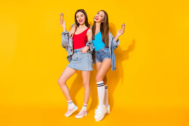 Full body photo positive cheerful girls sisters youth enjoy spring time weekend hold tasty icecream scoops wear red blue tank-top denim legs long socks isolated bright shine color background - Fotó, kép